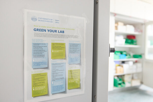 Foto: Ein Poster an einer Tür im Labor der Universität Hohenheim zeigt Tipps zur Verbesserung der Nachhaltigkeit im Labor. Der Text enthält Anweisungen zur Energieeinsparung und umweltfreundlichen Praktiken.