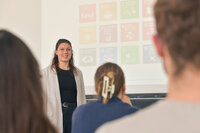 Foto: Eine Person steht vor einer Präsentation mit Symbolen der UN-Nachhaltigkeitsziele. Im Vordergrund sind unscharf Personen im Publikum zu sehen.