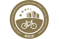 Infografik: Ein goldenes Abzeichen mit einem Fahrrad und Gebäuden, umgeben von Sternen. Text: 'ADFC-Zertifizierter fahrradfreundlicher Arbeitgeber nach EU-weitem Standard'.