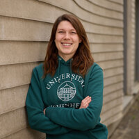Foto: Eine Person steht vor einer Wand und trägt einen grünen Hoodie mit dem Aufdruck 'Universität Hohenheim'.