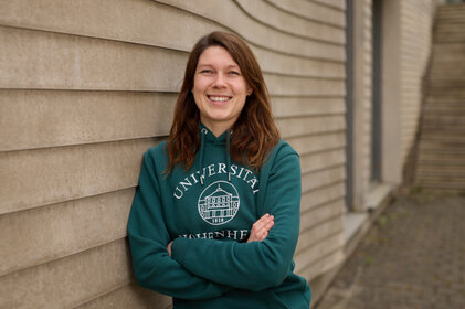 Foto: Eine Person steht vor einer Wand und trägt einen grünen Hoodie mit dem Aufdruck 'Universität Hohenheim'.