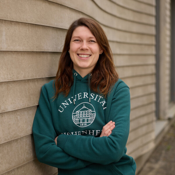 Foto: Eine Person steht vor einer Wand und trägt einen grünen Hoodie mit dem Aufdruck 'Universität Hohenheim'.