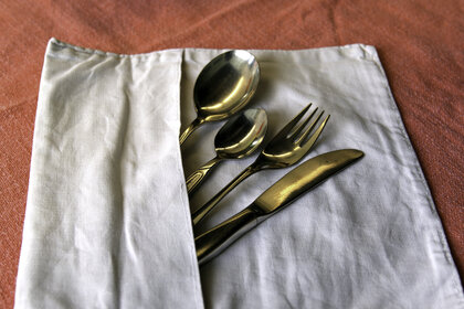 Foto: Ein Messer, eine Gabel und zwei Löffel sind in eine weiße Serviette eingewickelt, die auf einer roten Tischdecke liegt.